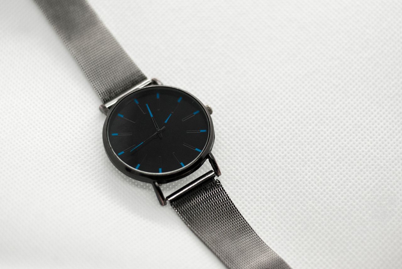 Minimalist silver wristwatch with mesh strap placed on a white textured surface for fashion and timekeeping themes.